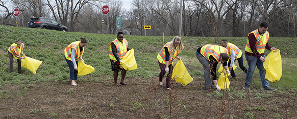 Volunteers in yellow vests picking up litter in a grassy area